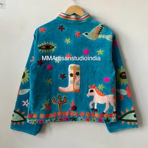 May include: Teal velvet jacket with colorful embroidered details. Features a bird, horse, cactus, and star designs. The jacket has a rainbow collar and the text "MMArtisanstudioindia".