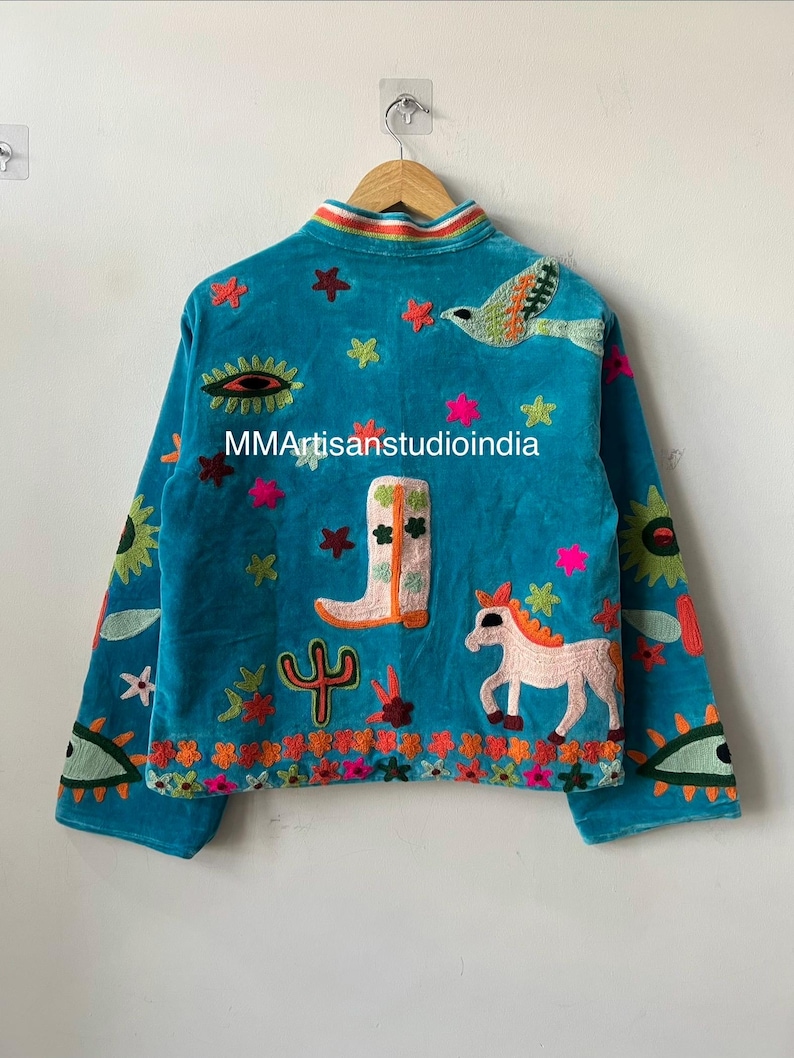 May include: Teal velvet jacket with colorful embroidered details. Features a bird, horse, cactus, and star designs. The jacket has a rainbow collar and the text "MMArtisanstudioindia".
