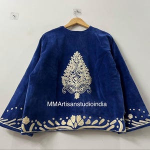May include: A royal blue jacket featuring a central cream-colored embroidered tree motif on the back. The hem and sleeve cuffs are decorated with cream-colored floral and dot embroidery. The text MMArtisanstudioindia is printed in white.