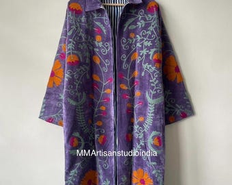 May include: A long-sleeved purple coat featuring vibrant orange and pink floral embroidery throughout the fabric. The garment has a classic collar and an open front design, revealing a black and white striped lining. Text reads MMArtisanstudioindia.