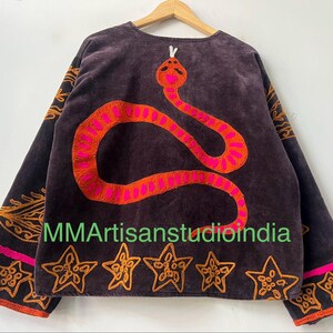 Puede incluir: Chaqueta marr&oacute;n oscuro con un gran dise&ntilde;o de serpiente bordada en naranja y rosa en la espalda. La chaqueta tiene bordados de estrellas y flores naranjas en la parte inferior y en las mangas. El texto "MMArtisanstudioindia" es visible.