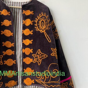 Puede incluir: Chaqueta de terciopelo marr&oacute;n oscuro con detalles bordados en naranja. La chaqueta presenta un forro a rayas y est&aacute; adornada con varias formas bordadas, incluyendo dise&ntilde;os tipo caramelo y patrones de estrellas. Las mangas tienen un ribete rosa.