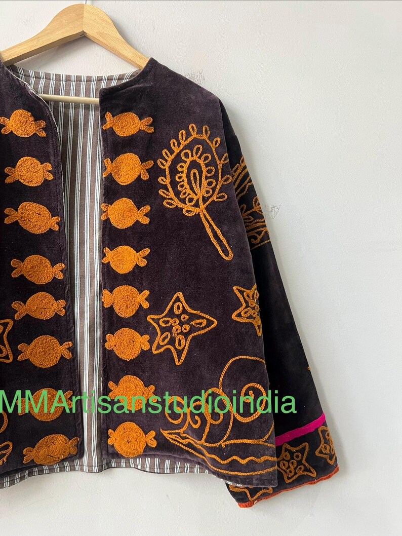 Puede incluir: Chaqueta de terciopelo marr&oacute;n oscuro con detalles bordados en naranja. La chaqueta presenta un forro a rayas y est&aacute; adornada con varias formas bordadas, incluyendo dise&ntilde;os tipo caramelo y patrones de estrellas. Las mangas tienen un ribete rosa.