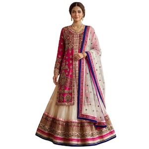 Puede incluir: Un vestido indio magenta y crema ornamentado. La parte superior de manga larga presenta intrincados bordados dorados, y la falda tiene un diseño a juego. Una bufanda blanca transparente con ribetes rosas y azules completa el conjunto.