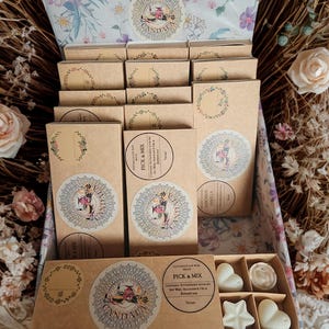 May include: A decorative box filled with handmade soy wax melts. The box contains several small, rectangular boxes with floral designs and circular stickers. The bottom box holds heart and star-shaped wax melts. The text "PICK & MIX" is visible.