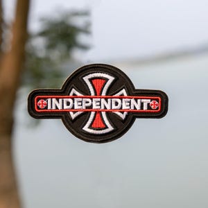 May include: An embroidered patch in black and red, featuring the word "INDEPENDENT" in white. The design includes a cross motif with red and white detailing. The patch has a circular shape with a rectangular bar across the middle.