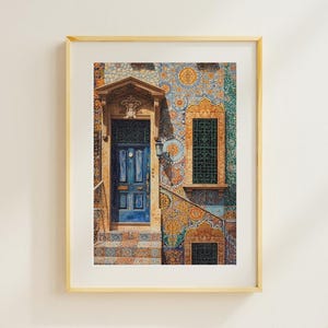 May include: A framed print of a building facade with a blue door and intricate mosaic tilework in shades of blue, orange, and yellow. The artwork captures the architectural details of the building, including the door, window, and stairs.