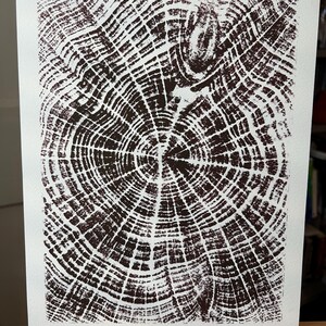 Könnte beinhalten: Ein braun-weißer Druck eines Baumquerschnitts, der konzentrische Ringe und komplizierte Muster zeigt. Das Kunstwerk wird auf weißem Papier präsentiert und fängt die natürliche Textur und die Details der Holzmaserung ein. Der Druck zeigt die Jahresringe des Baumes.