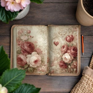 May include: Open vintage journal with floral rose illustrations in shades of pink and burgundy. A small red heart is featured on the right page. An orange pen rests beside the journal on a dark wood surface.