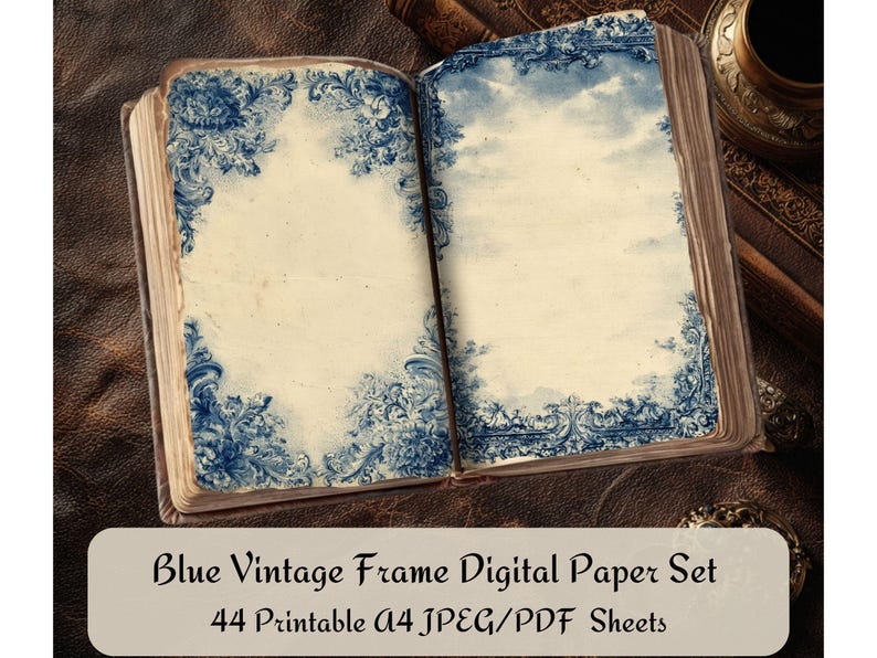 May include: An open book with aged pages featuring blue floral frame designs. The text "Blue Vintage Frame Digital Paper Set" is displayed on a white oval. The book is on a brown leather surface, with other books and a decorative object in the background.