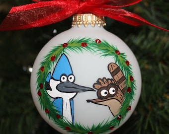 Handpainted Glass Personalized Ornament with the Regular Shows Mordecai and Rigby peeking through a Christmas wreath