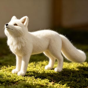 May include: A handcrafted white fox figurine with a fluffy texture, standing on a bed of green moss. The fox is looking upwards with its amber eyes. The figurine is made of a soft, wool-like material.