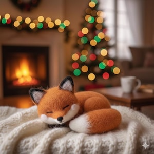 May include: A handcrafted orange fox plush toy with a white belly and tail, and black-tipped ears, is curled up asleep on a white knitted blanket. The background features a fireplace, Christmas tree, and festive lights, creating a cozy holiday scene.