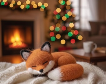 Puede incluir: Un peluche artesanal de zorro naranja con vientre y cola blancos, y orejas con puntas negras, está acurrucado durmiendo sobre una manta de punto blanca. El fondo presenta una chimenea, un árbol de Navidad y luces festivas.