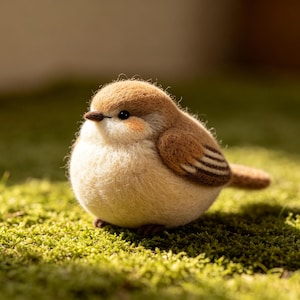 May include: A handcrafted felt bird figurine with a rounded body, featuring a light brown head and wings, a cream-colored chest, and a small, dark beak. The bird is set on a bed of green moss, with soft lighting.