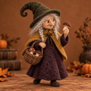 Puede incluir: Una muñeca de lana fieltrada de una figura anciana con cabello gris, que lleva un sombrero puntiagudo verde oscuro, una capa amarillo mostaza y un vestido morado oscuro. La figura sostiene un pequeño hongo marrón y lleva una cesta tejida con dos hongos.