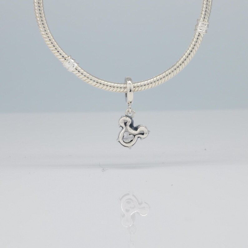 Puede incluir: Un charm de plata con forma de ampersand, colgado de una cadena plateada. El charm, con un acabado pulido, se presenta sobre un fondo claro. Es una pieza de joyer&iacute;a.