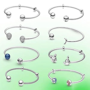May include: A collection of silver-toned bracelets with various decorative charms. Charms include spheres, sparkling beads, a moon, a Mickey Mouse head, and other designs. The bracelets are displayed on a gradient green background.