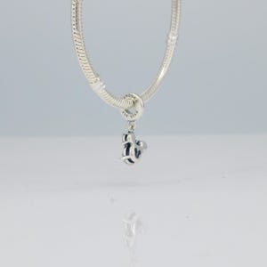 Puede incluir: Un charm de plata con un dise&ntilde;o de Mickey Mouse cuelga de una pulsera de plata. El charm est&aacute; detallado con detalles en negro y la pulsera tiene un dise&ntilde;o de cadena de serpiente. El charm est&aacute; marcado con el nombre de la marca "Pandora".