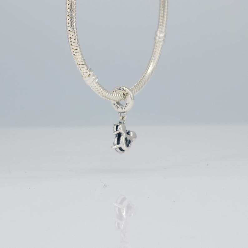 Puede incluir: Un charm de plata con un dise&ntilde;o de Mickey Mouse cuelga de una pulsera de plata. El charm est&aacute; detallado con detalles en negro y la pulsera tiene un dise&ntilde;o de cadena de serpiente. El charm est&aacute; marcado con el nombre de la marca "Pandora".