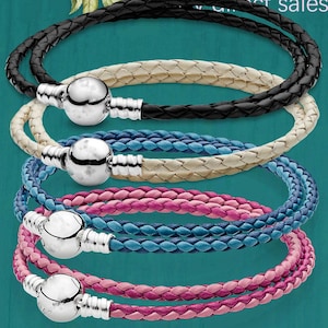 Puede incluir: Pulseras envolventes de cuero trenzado en negro, crema, azul y rosa. Cada pulsera presenta un cierre plateado. Las pulseras se exhiben sobre un fondo turquesa, mostrando sus colores y texturas.