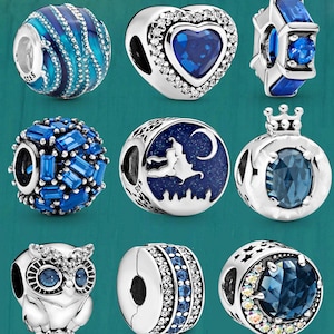 May include: A collection of silver charm beads with blue accents. Designs include a heart, a crown, an owl, and beads with blue crystals. Some beads have a witch and moon design.