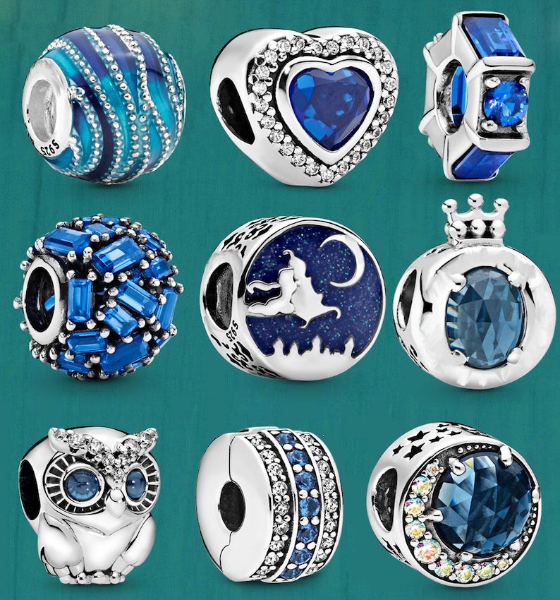 May include: A collection of silver charm beads with blue accents. Designs include a heart, a crown, an owl, and beads with blue crystals. Some beads have a witch and moon design.