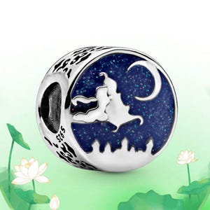 May include: A silver charm with a blue enamel design featuring a silhouette of a couple, a crescent moon, and a cityscape. The charm has a starry night sky background and the text "S925". The charm is round with a patterned edge.
