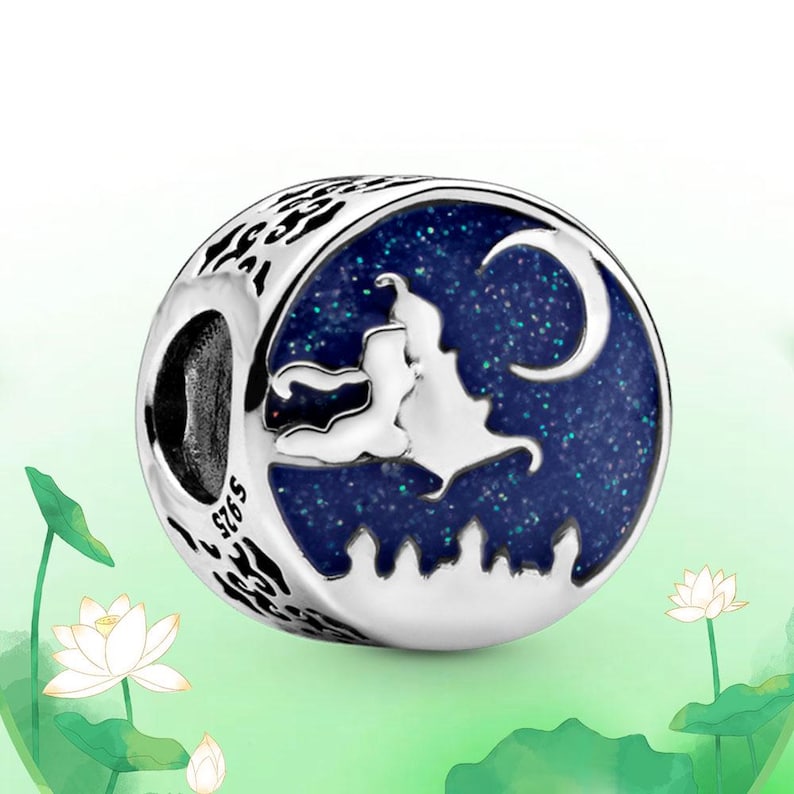 May include: A silver charm with a blue enamel design featuring a silhouette of a couple, a crescent moon, and a cityscape. The charm has a starry night sky background and the text "S925". The charm is round with a patterned edge.