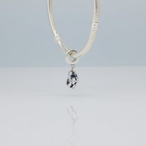 Puede incluir: Un charm de plata con un dise&ntilde;o de Mickey Mouse, colgando de una cadena de plata. El charm presenta una representaci&oacute;n detallada de la silueta de Mickey Mouse, con detalles de esmalte negro. La cadena es de estilo cl&aacute;sico de cadena de serpiente, y el charm es probablemente una joya.