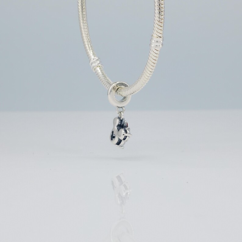 Puede incluir: Un charm de plata con un dise&ntilde;o de Mickey Mouse, colgando de una cadena de plata. El charm presenta una representaci&oacute;n detallada de la silueta de Mickey Mouse, con detalles de esmalte negro. La cadena es de estilo cl&aacute;sico de cadena de serpiente, y el charm es probablemente una joya.