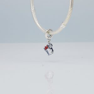 Puede incluir: Un charm de plata con un dise&ntilde;o de Minnie Mouse, con una piedra clara facetada y un lazo rojo. El charm est&aacute; suspendido de una pulsera de plata. Es una joya.