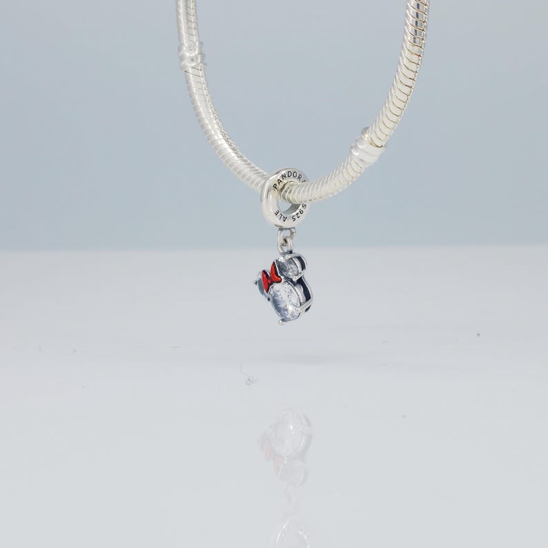 Puede incluir: Un charm de plata con un dise&ntilde;o de Minnie Mouse, con una piedra clara facetada y un lazo rojo. El charm est&aacute; suspendido de una pulsera de plata. Es una joya.