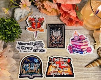 Puede incluir: Una colección de pegatinas con diseños y textos temáticos de libros. Las pegatinas incluyen frases como "Enemies to Lovers", "Morally Grey is my favorite color" y "The Smut Reader". La paleta de colores incluye rosa, azul y negro.