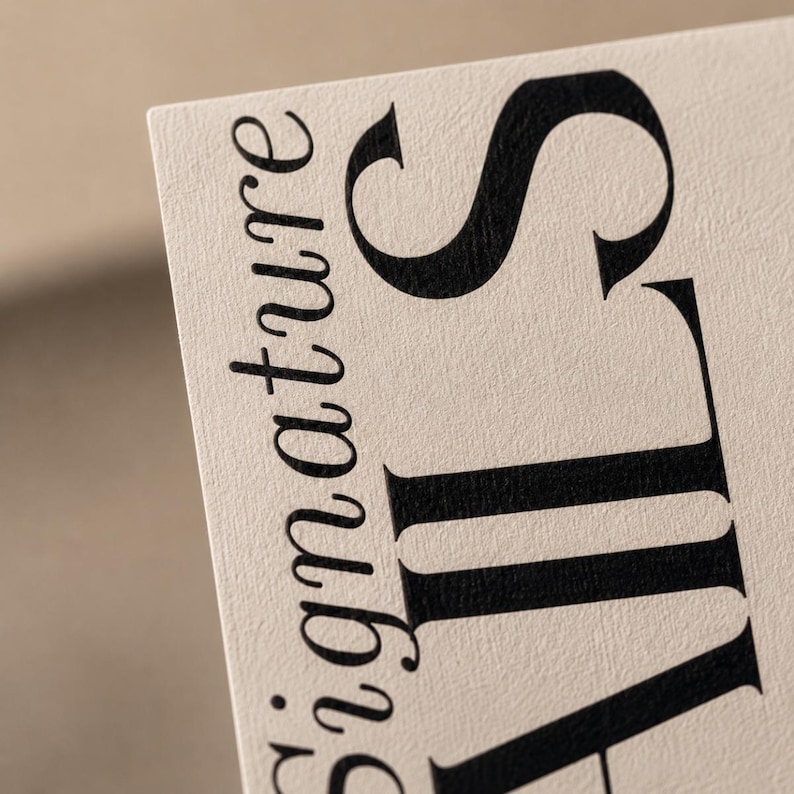 Op de afbeelding: Close-up van een beige visitekaartje met het woord "signature" in een zwart, elegant lettertype. Het woord "signature" is verticaal geori&euml;nteerd, met de letter "S" prominent weergegeven.