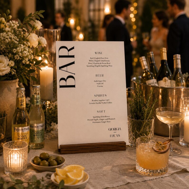 Op de afbeelding: Een drankmenu op een houten standaard, met het woord "BAR" in grote, zwarte letters. Het menu bevat wijn, bier, sterke drank en frisdranken. De tafel is gedekt met drankjes, olijven, citroenen en kaarsen.
