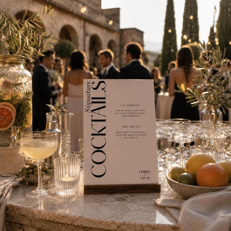 Op de afbeelding: Een cocktailbar met een menubord met de tekst "Signature Cocktails". Het menu bevat twee cocktails, "La Giorgia" en "The Lucan". Een kom met citrusvruchten en een cocktailglas staan op het marmeren aanrecht. De achtergrond toont een bijeenkomst.