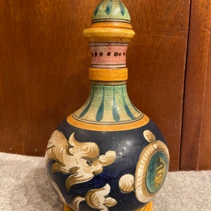 May include: A hand-painted ceramic bottle with a blue and yellow glaze. The bottle has a round body with a narrow neck and a decorative lid. The bottle is decorated with floral and geometric patterns.