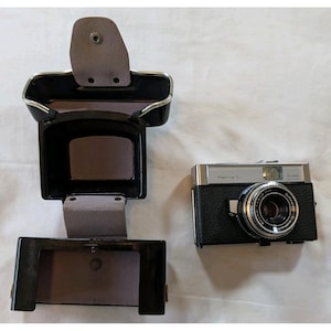 May include: A vintage Retina S1 camera with a black leather case. The camera has a silver top and a black body with a lens. The case is open, revealing a gray interior. The camera is a classic photography item.
