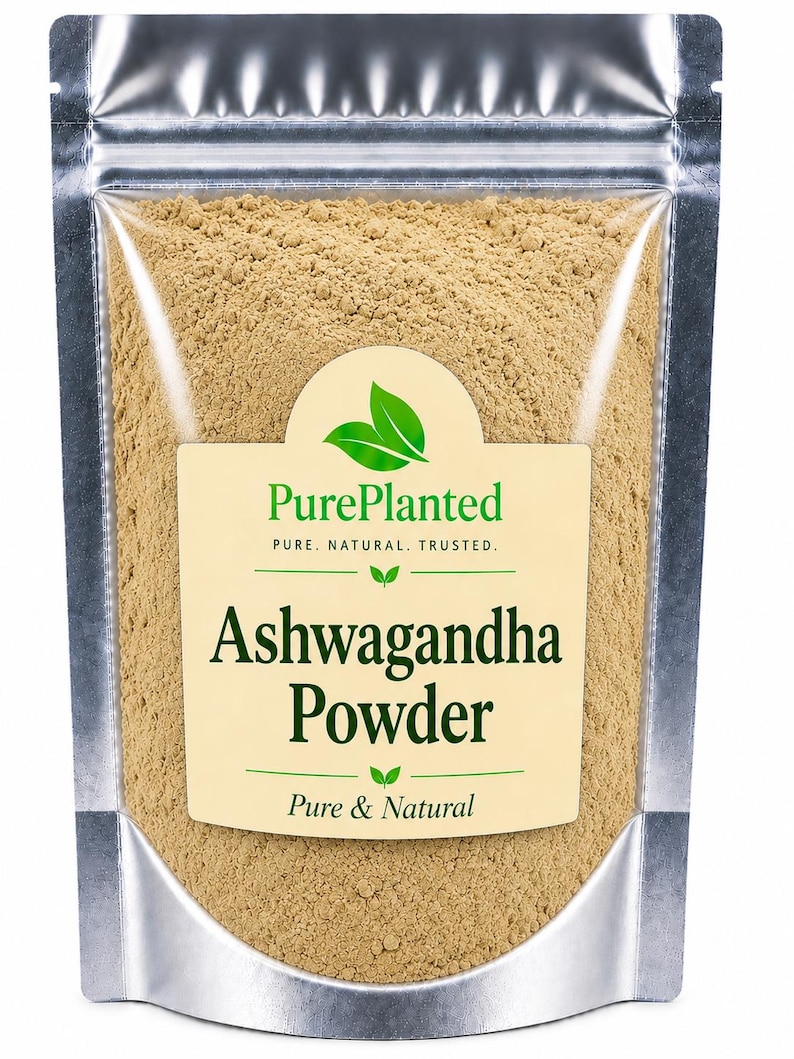 May include: A silver pouch filled with light brown ashwagandha powder. The pouch has a clear window and a label with the text "PurePlanted" and "Ashwagandha Powder". The label also states "Pure & Natural".