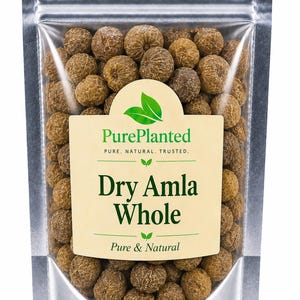 Op de afbeelding: Een transparante zak met zilveren rand gevuld met gedroogde amla-bessen. Het etiket luidt "PurePlanted" en "Dry Amla Whole, Pure & Natural". De bruine bessen zijn rond en hebben een textuur. De zak is verzegeld.