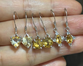 Puede incluir: Una colección de pendientes colgantes de plata con piedras preciosas amarillas. Los pendientes presentan piedras en forma de corazón, redondas y de estrella. Las piedras tienen un tono dorado cálido.