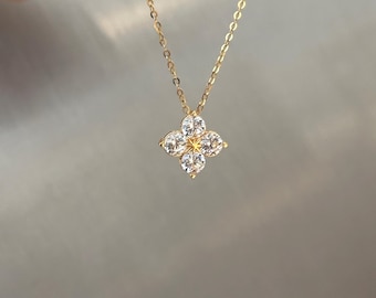 Puede incluir: Un collar dorado con un colgante de trébol de cuatro hojas. El colgante presenta cuatro piedras preciosas redondas y transparentes que rodean un diseño de estrella dorada más pequeño. La cadena es delicada y dorada.