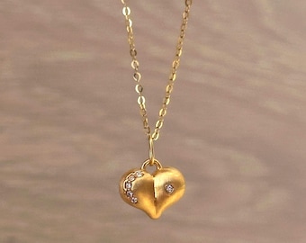 Puede incluir: Un collar con colgante de corazón dorado. El dije en forma de corazón está adornado con pequeñas piedras preciosas transparentes y cuelga de una delicada cadena dorada. Una joya romántica.