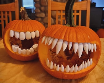May include: Two carved orange pumpkins with large, white teeth, resembling open mouths. The pumpkins are on a wooden surface, with a glimpse of a wooden chair and a stone wall in the background. A Halloween theme.