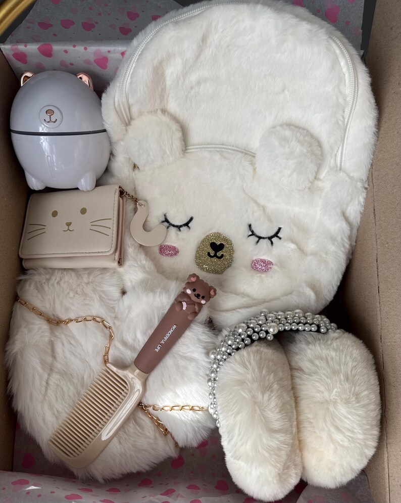 Puede incluir: Una colecci&oacute;n de accesorios de felpa blanca, que incluye una mochila con forma de oso, una peque&ntilde;a cartera con cara de gato, un peine y una diadema con perlas. Tambi&eacute;n hay un peque&ntilde;o recipiente blanco con tem&aacute;tica de oso.