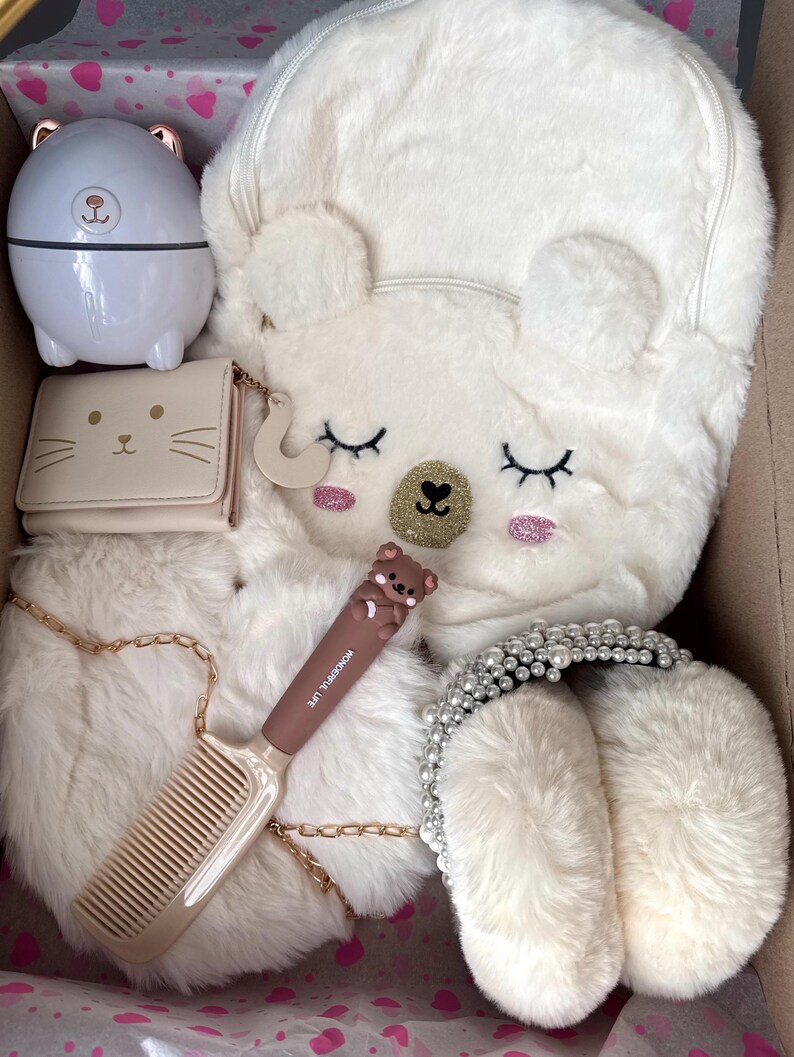 Puede incluir: Una colecci&oacute;n de accesorios blancos y beige, que incluye una mochila con orejas de oso, una cartera con cara de gato, un peine, una diadema y un peque&ntilde;o recipiente con forma de oso. Los art&iacute;culos est&aacute;n dispuestos en una caja de cart&oacute;n.