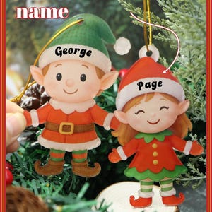 Può includere: Due decorazioni natalizie a forma di elfo, una con cappello verde e il nome "George", l'altra con cappello rosso e il nome "Page". Entrambi indossano abiti arancioni e verdi. Il testo "Customized name" è in alto.