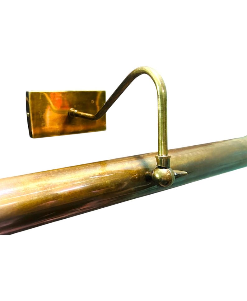 May include: A vintage-style brass picture light. The light features a rectangular wall mount, a curved arm, and a cylindrical light fixture. The brass has a warm, aged patina. The design is simple and elegant, suitable for illuminating artwork.