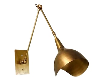 May include: A brass wall-mounted lamp with an adjustable arm and a conical shade. The lamp has a rectangular base and a pivoting arm that allows for directional lighting. The shade is a warm gold color.